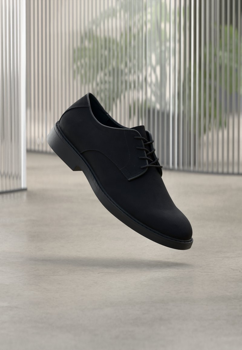 Μαύρο επίσημο παπούτσι από λείο υλικό, με στρογγυλεμένη μύτη, σχέδιο με κορδόνια και ανθεκτική μαύρη σόλα, παρουσιασμένο να αιωρείται στον αέρα.