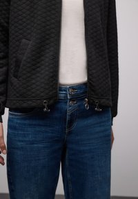 Czarna pikowana kurtka z zamkiem błyskawicznym i ściągaczem, zestawiona z niebieskimi dżinsami z dwuguzikowym zapięciem i subtelnymi detalami przeszyć.