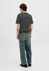 Sort og hvid stribet t-shirt med korte ærmer, parret med l�øse, falmede blå jeans. Sorte sko synlige. Ensfarvet baggrund.