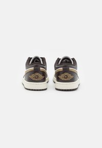 Sneaker in pelle marrone con una suola intermedia bianca rialzata, colletto imbottito e logo dorato a forma di ala sul tallone. Punta arrotondata, lacci piatti e suola testurizzata.