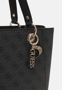 Geantă tote neagră cu țesătură texturată, având un model cu logo-uri. Elemente din metal auriu, inclusiv un inel pentru chei și etichete, adaugă detaliu.