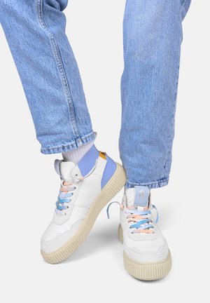 Weiße Sneaker mit pastellblauen und rosanen Schuhbändern, strukturiertem Gummisohle und blauen Akzenten an der Ferse, kombiniert mit hellblauen Jeans.
