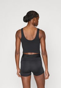 Μαύρο κοντό τοπ χωρίς μανίκια με φαρδιές τιράντες και λείο φινίρισμα, σε συνδυασμό με μαύρο αθλητικό σορτς ψηλόμεσο με υφασμένη ζώνη μέσης.