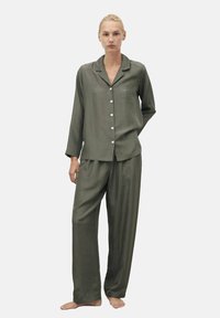 Olivgrünes, langärmliges Pyjama-Set mit einem knopfbaren Oberteil mit Tasche und locker sitzenden, geraden Hosen. Glatte Textur und subtile Anmutung.