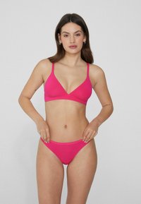 Ensemble bikini rose comprenant un haut bralette triangulaire à bretelles ajustables et un bas string taille basse. Tissu lisse et extensible.