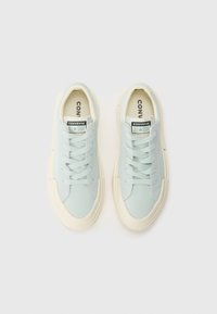 Világoskék vászon sportcipők kerek orral, fehér gumitalppal és megkötős záródással. A nyelvén Converse All Star logó található.