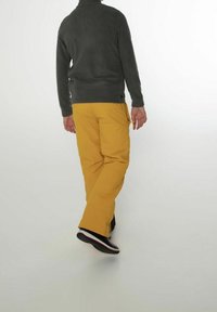 Polarowa kurtka w ciemnoszarym kolorze, zestawiona z żółtymi spodniami narciarskimi. Spodnie mają kieszenie typu cargo; obuwie jest czarne z białą podeszwą i czerwonymi akcentami.