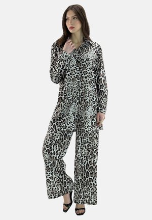 Femme aux longs cheveux bruns portant une chemise ample à boutons imprimé léopard et un pantalon large assorti, avec des talons ouverts noirs.