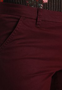 Bordeauxkleurige broek van soepel materiaal met een getailleerd ontwerp, voorzien van een standaard tailleband, zijzakken en nette stiksels.