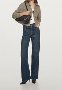 Cardigan tricoté vert olive, haut blanc, jean en denim foncé taille haute à jambes larges, sac à bandoulière en cuir noir avec talons pointus noirs.