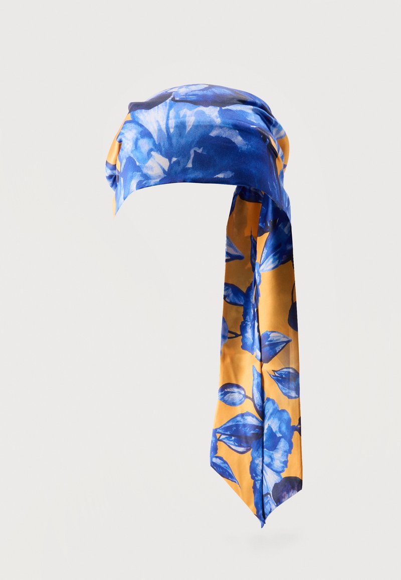 Μεταξωτό μαντήλι με μπλε λουλουδένια σχέδια σε κίτρινο φόντο, δεμένο χαλαρά με μακριά κρεμαστά άκρα.