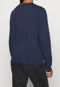 Granatowa bluza z okrągłym dekoltem, długimi rękawami i prążkowanymi mankietami. Posiada trójkątny tylny karczek oraz luźny krój.