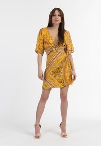 Rochie galbenă cu model, cu mâneci scurte, decolteu în V adânc și o decupare circulară la talie. Prezintă spirale și accente cu print de leopard.