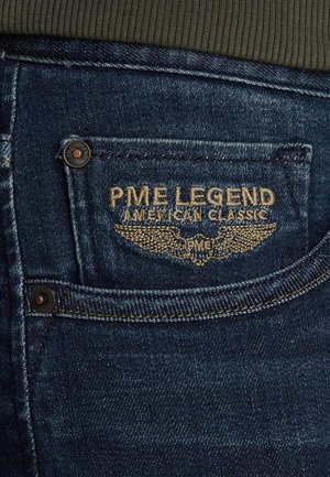 Traperice tamnoplave boje, s stražnjim džepom na kojem se nalazi zlatno izvezeni logo "PME Legend American Classic" i metalni ukras dugmetom.