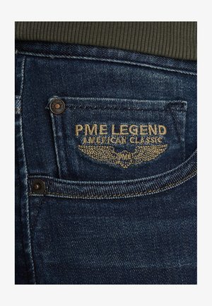 Traperice tamnoplave boje, s stražnjim džepom na kojem se nalazi zlatno izvezeni logo "PME Legend American Classic" i metalni ukras dugmetom.