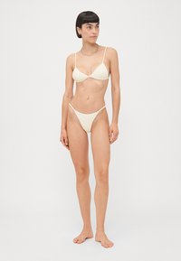 Crème-kleurige bikini set met een driehoekige bikini top met dunne bandjes en bijpassende minimalistische hoog-getailleerde broekjes. Zachte textuur.
