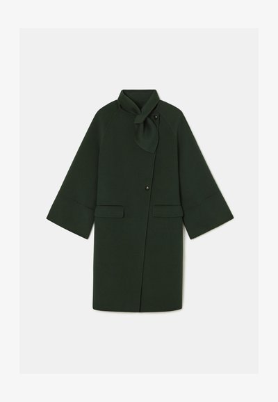 Mørkegrøn frakke med en omslag design, der har en knytterneck, store forlommer og brede ærmer. Fremstillet af blødt stof med en glat tekstur.