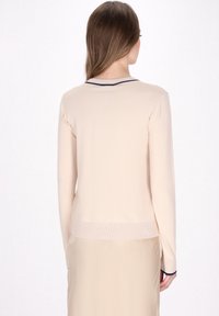Beige geribbelde gebreide trui met lange mouwen en een marineblauwe kraagdetails. Heeft een getailleerde pasvorm en een rechte zoom op de taille.