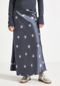 Personne portant une jupe maxi gris foncé avec des étoiles blanches, un haut gris à manches longues et des baskets argentées avec des lacets blancs et des semelles en gomme.