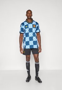 Blå og hvid ternet fodboldtrøje med sort krave, prydet med logoer og detaljer; parret med sorte shorts og stribede sokker.