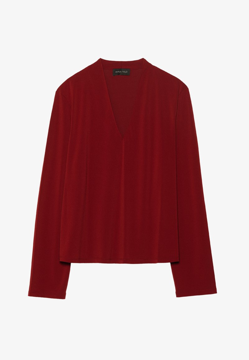 Rdeča majica z dolgimi rokavi, izdelana iz mehkega materiala, z globokim V-izrezom in sproščenim krojem. Gladka, minimalistična tekstura brez vidnih vzorcev.