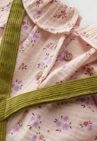 Blumendekorierter, hellrosa Stoff mit kleinen lila und orangen Blumen; verfügt über einen grünen Rippkragen und Knopfdetails.