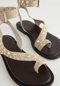 Beige suède sandalen met ronde metalen accenten, T-band ontwerp en verstelbare enkelgesp. Bruine rubberen zool voor comfort.
