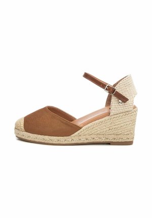 Sandale compensée marron avec semelle en corde tressée, dessus de talon tissé et bride de cheville réglable avec boucle argentée sur fond blanc.