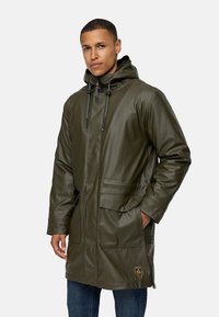 Olijfgroene waterdichte parka met een capuchon, voorzien van twee voorzakken en verstelbare trekkoorden. Glad materiaal, knielange stijl.