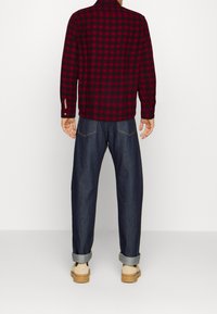 Camicia a quadri rossa e nera in flanella, maniche lunghe, abbinata a jeans di denim scuro larghi, con i polsini arrotolati e scarpe beige slip-on.