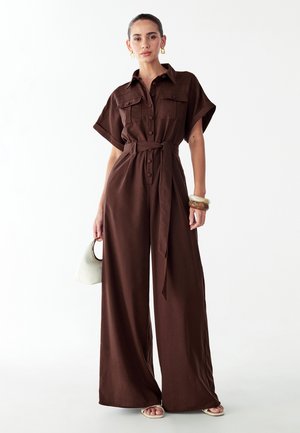 Brun linnedragt med korte ærmer, knapper foran og bælte i taljen. Har vide ben og en glat tekstur. Inkluderer en off-white håndtaske.