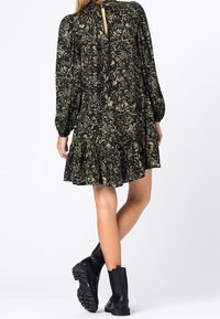 Vestido negro con estampado floral verde, mangas largas abullonadas, dobladillo en capas y detalle de ojal en la espalda, combinado con botas negras hasta el tobillo.