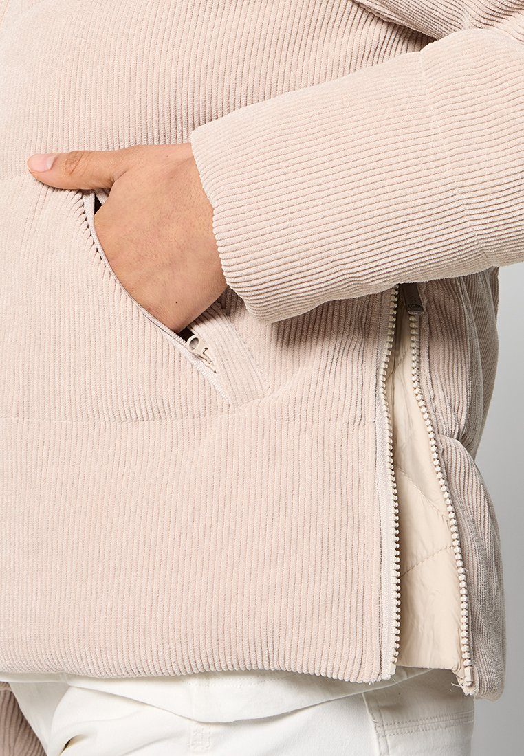 Helle rosa Cordjacke mit seitlichen Reißverschlusstaschen und gestepptem Innenfutter. Verfügt über eine gerippte Textur und ein tailliertes Manschettendesign.