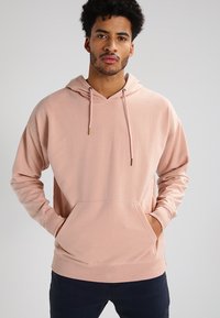 Felpa leggera rosa chiaro realizzata in tessuto morbido, con tasca frontale, cappuccio regolabile con cordino e polsini a coste. Vestibilità standard con maniche lunghe.