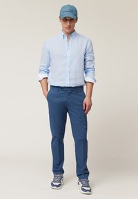 Chemise en lin bleu clair, pantalon bleu et casquette bleue avec logo. Les baskets présentent des accents blancs et bleus. Design simple avec des détails en boutons.