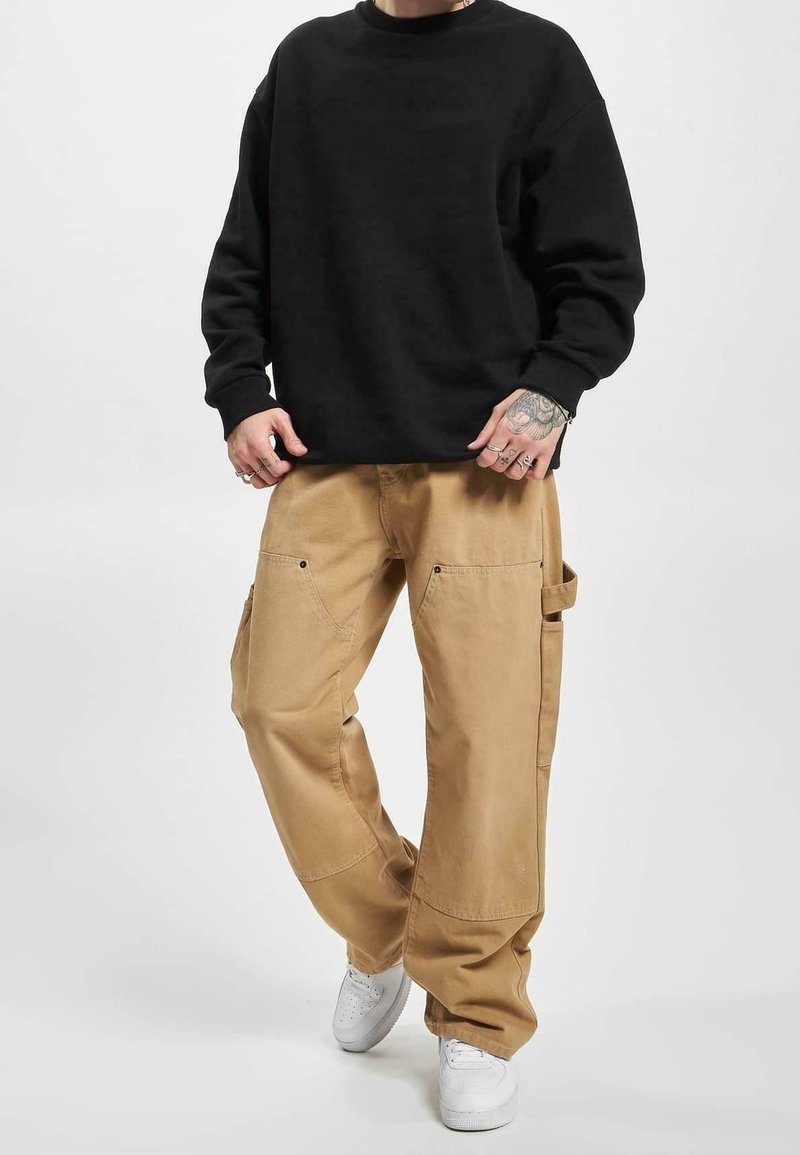 Sweat-shirt noir à manches longues, assorti à un pantalon cargo beige avec poches latérales. Des baskets blanches complètent la tenue.
