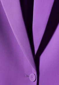 Tela de blazer morada con textura suave, que presenta un cuello con muesca y un detalle de botón redondo. La línea de costura añade estructura al diseño.