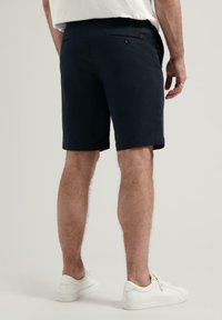 Marineblaue Baumwollkurze Hosen mit geradem Schnitt, zwei Gesäßtaschen mit Knöpfen und einem umgeschlagenen Saum. Getragen mit weißen Sneakers.