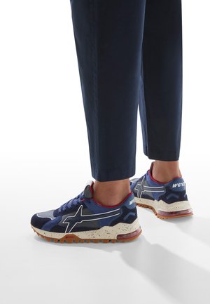 Sneakers blu navy realizzati in materiali scamosciati e mesh, con una suola intermedia bianca maculata, dettagli rossi e una suola in gomma dotata di dettagli per la trazione.