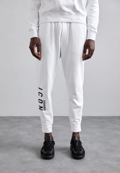 White sweatpants with a printed black "ICON" and brand logo on the side, elastic cuffs, paired with black sneakers. Smooth, casual fabric.