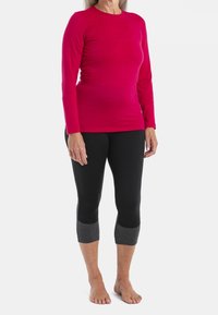 Farkku pitkähihainen paita kirkasta vaaleanpunaista materiaalia yhdistettynä mustiin leggings-housuihin, joissa on tummanharmaat nilkkakaitaleet. Molemmat vaatteet ovat saumattomia ja joustavia.