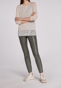 Lichtbeige top met lange mouwen en luipaardprint, over een witte en groene gestreepte onderhemd. Donkergroene glanzende leggings. Beige sneakers.
