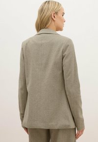 Blazer a spina di pesce color beige con vestibilità sartoriale, reverse a notche e tessuto testurizzato; cuciture delle spalle visibili e spacchi laterali all'orlo.