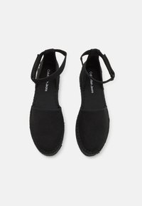 Chaussures espadrilles noires avec tige en toile, bout rond et bride de cheville ; semelle en corde texturée et doublure en tissu. Nom de la marque visible à l'intérieur.