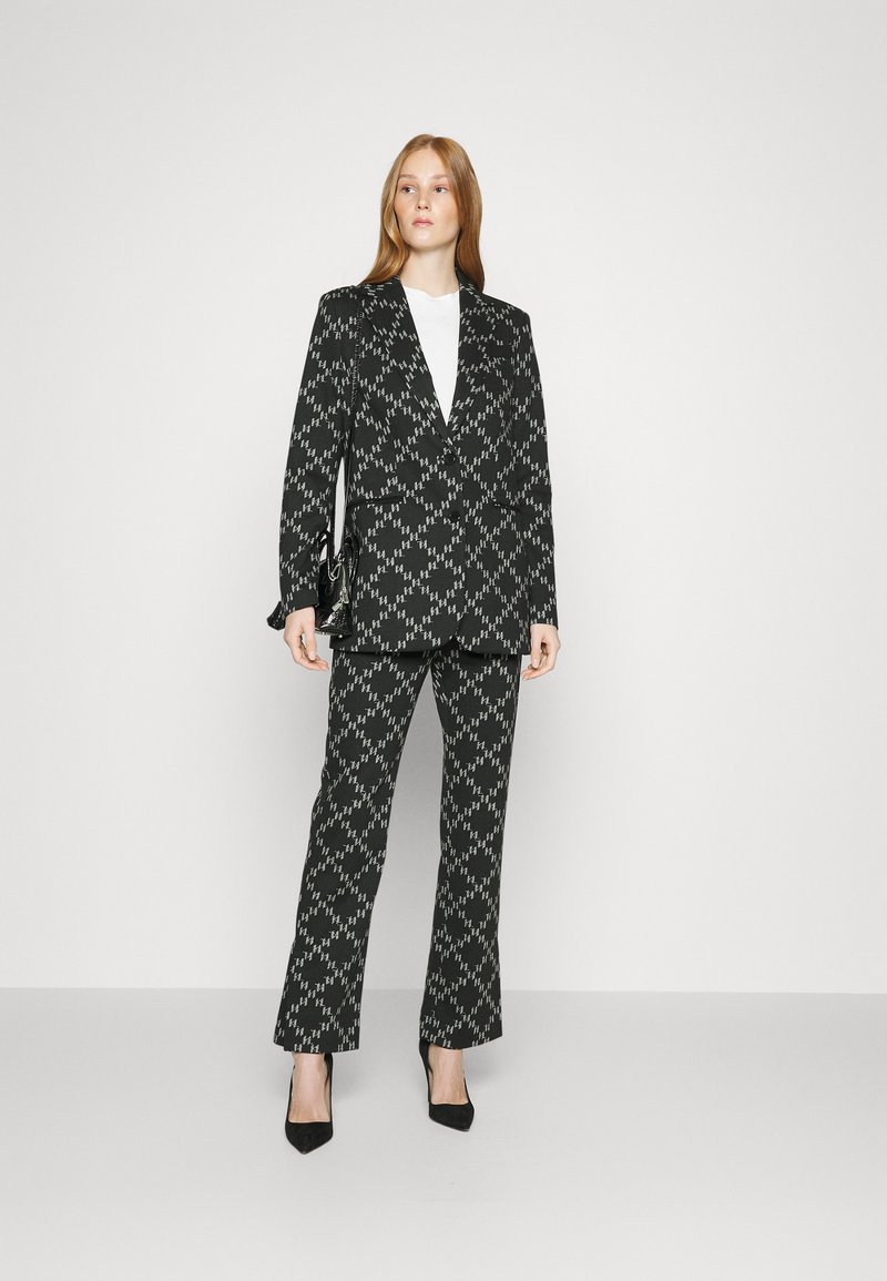 Completo giacca e pantaloni a motivi in bianco e nero, caratterizzato da un design strutturato e una texture liscia, abbinato a scarpe con tacco alto nere.