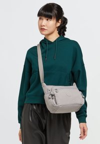 Borsa a tracolla grigia con tracolla regolabile, scomparti con zip e finitura in tessuto testurizzato. Presenta un logo discreto sul davanti.