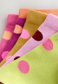 Cinq chaussettes pliées en tricot coloré avec de grands pois roses, rouges, pêche et violets sur des fonds verts, roses, moutarde, violets et oranges.