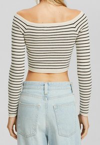 Top de rayas cream y negro, con escote off-the-shoulder y mangas largas, diseño cropped. Combinado con jeans de tiro alto en azul claro.