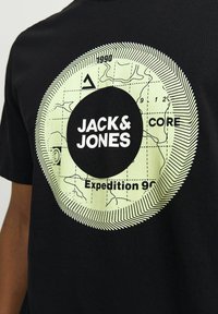 Zwarte katoenen t-shirt met een grote groene cirkelvormige graphic met een kaartontwerp, de tekst "JACK & JONES" en accenten in expeditiethema.