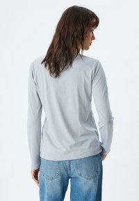 Lichtgrijze longsleeve shirt van zachte stof, met een ronde halslijn en getailleerde mouwen. Gecombineerd met hooggerokte spijkerbroek.